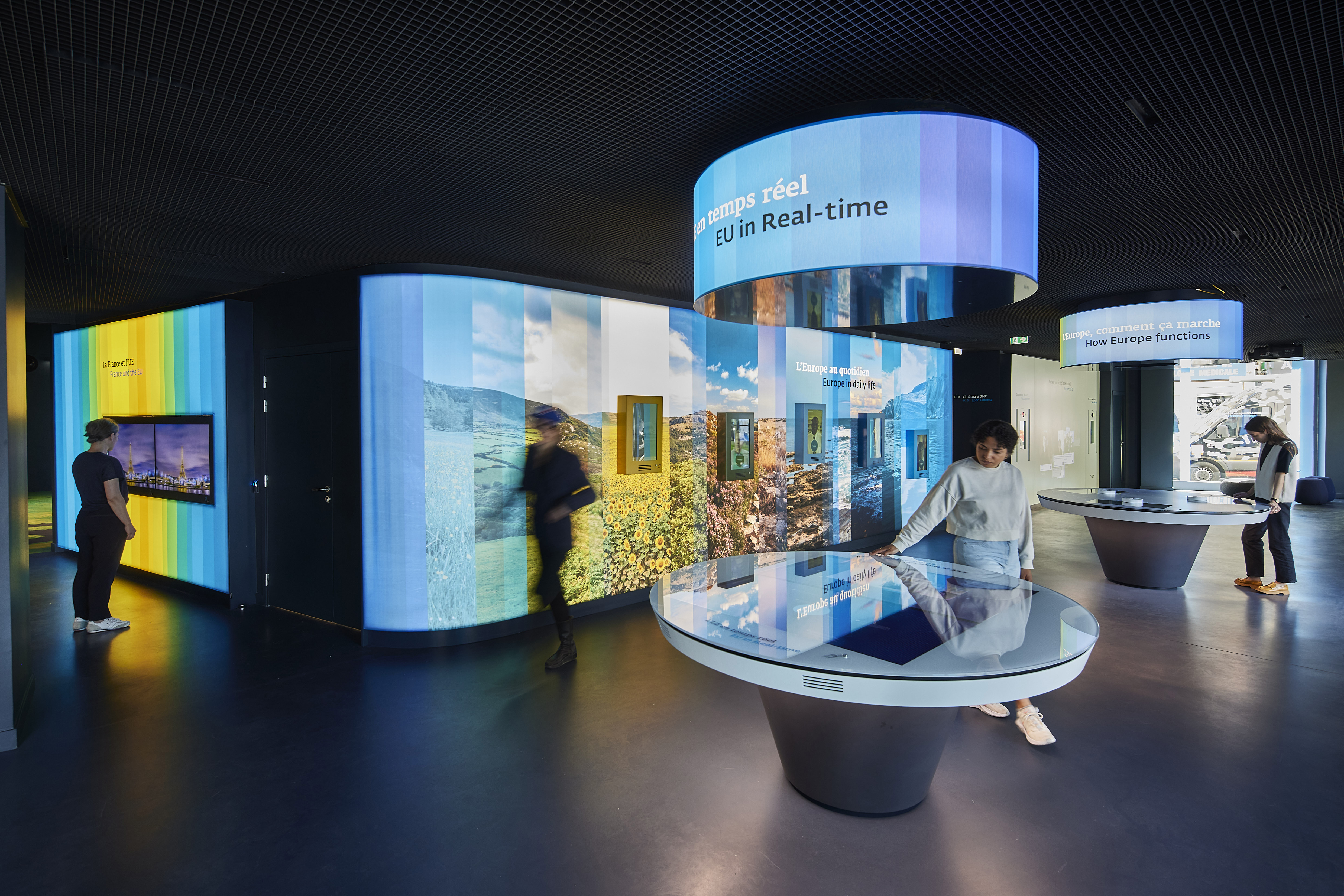 Intérieur de l'espace visiteurs Europa Expérience avec des tables rondes, murs colorés et écrans.