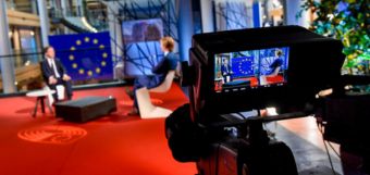 Le caméra film deux hommes assis sur les chaises devant un drapeau de l'Union européenne.